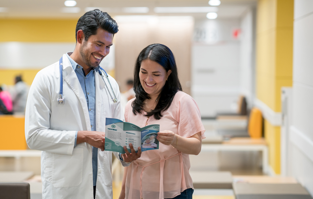 Cheerful woman talking to doctor about a retirement home for her parents while she looks at a brochure alternate text for this image