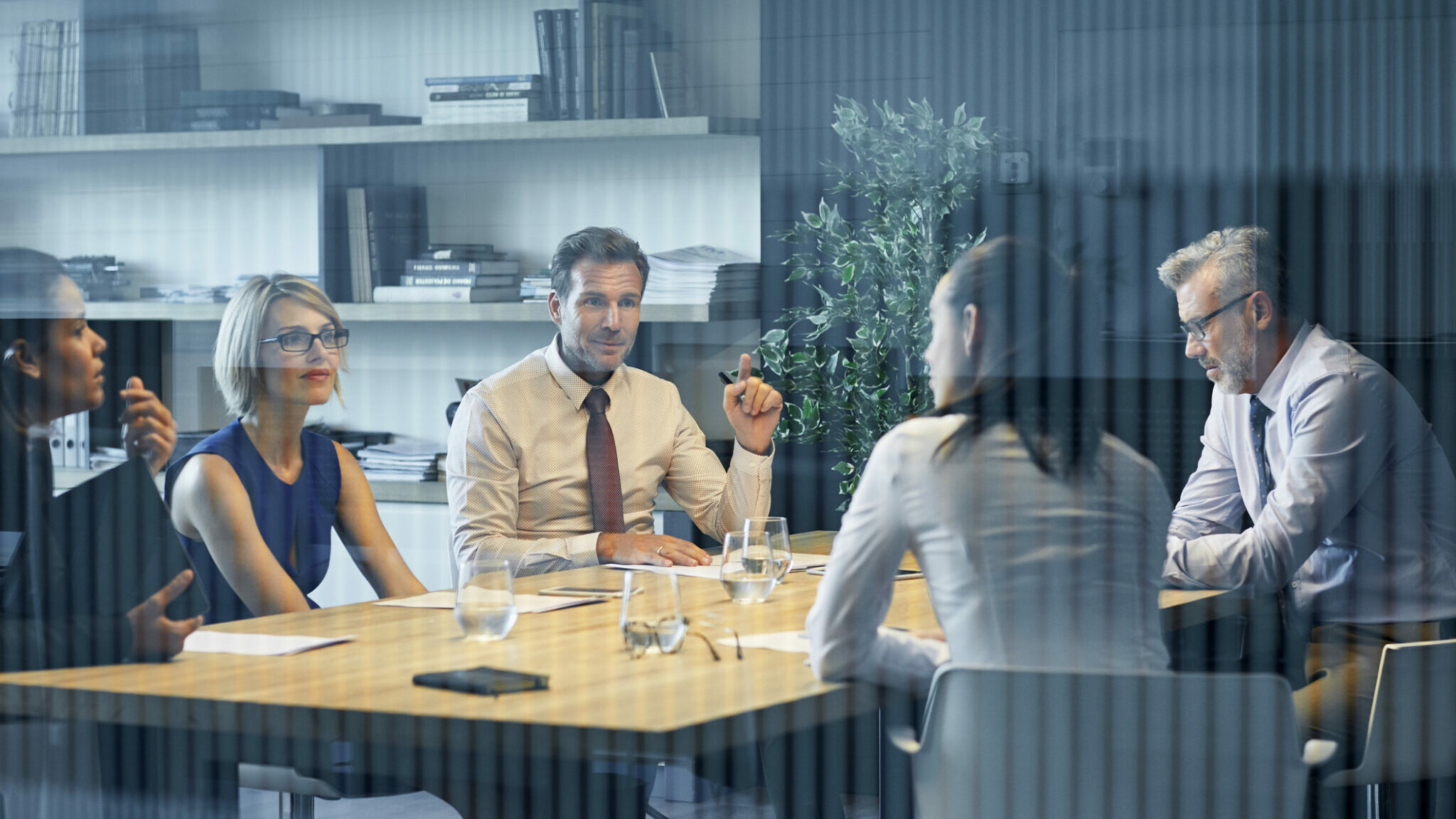 Coworkers communicating at desk seen through glass alternate text for this image