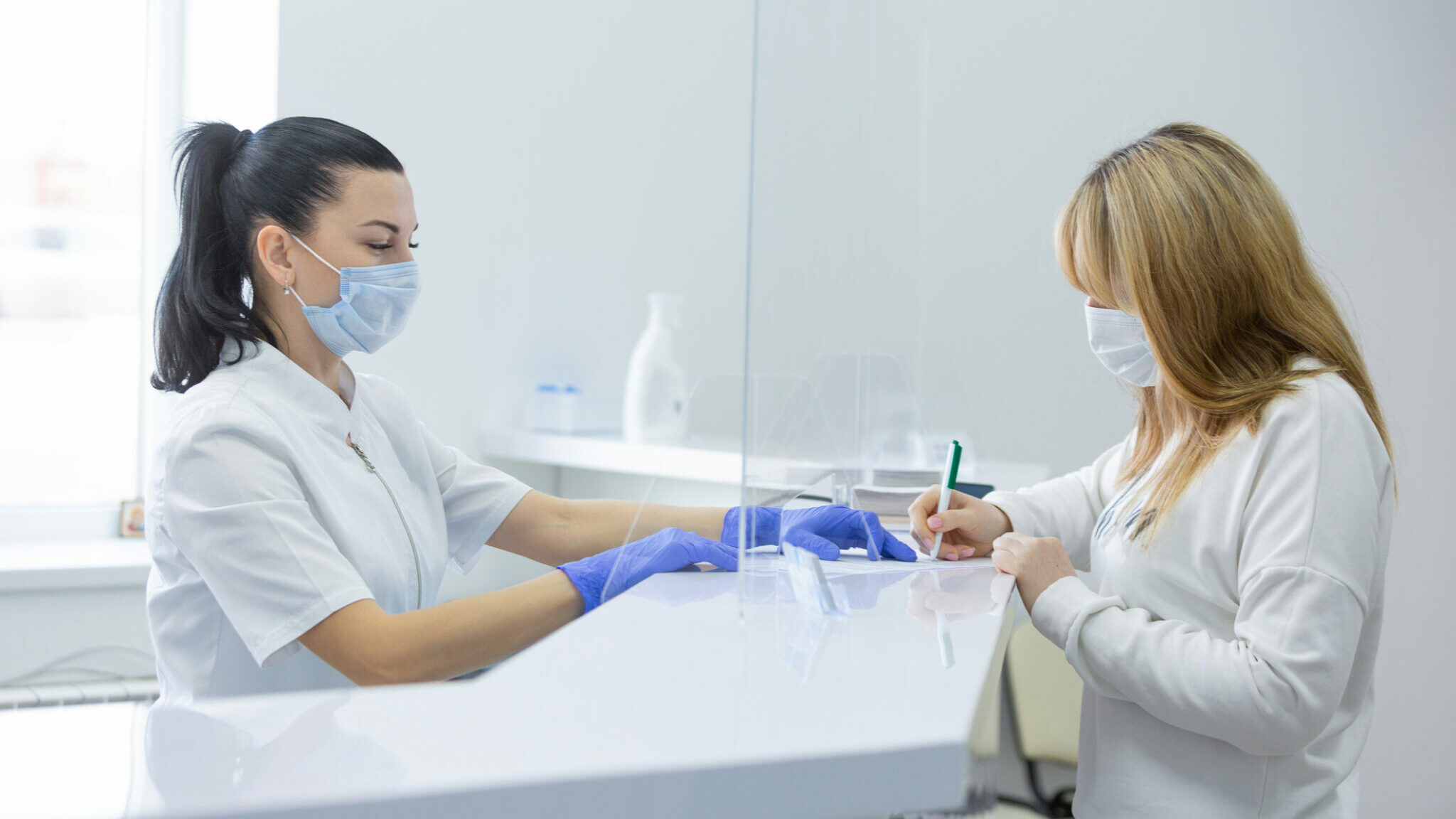 A receptionist in a modern hospital helps a young female patient fill out documents. Consent to the processing of personal data alternate text for this image