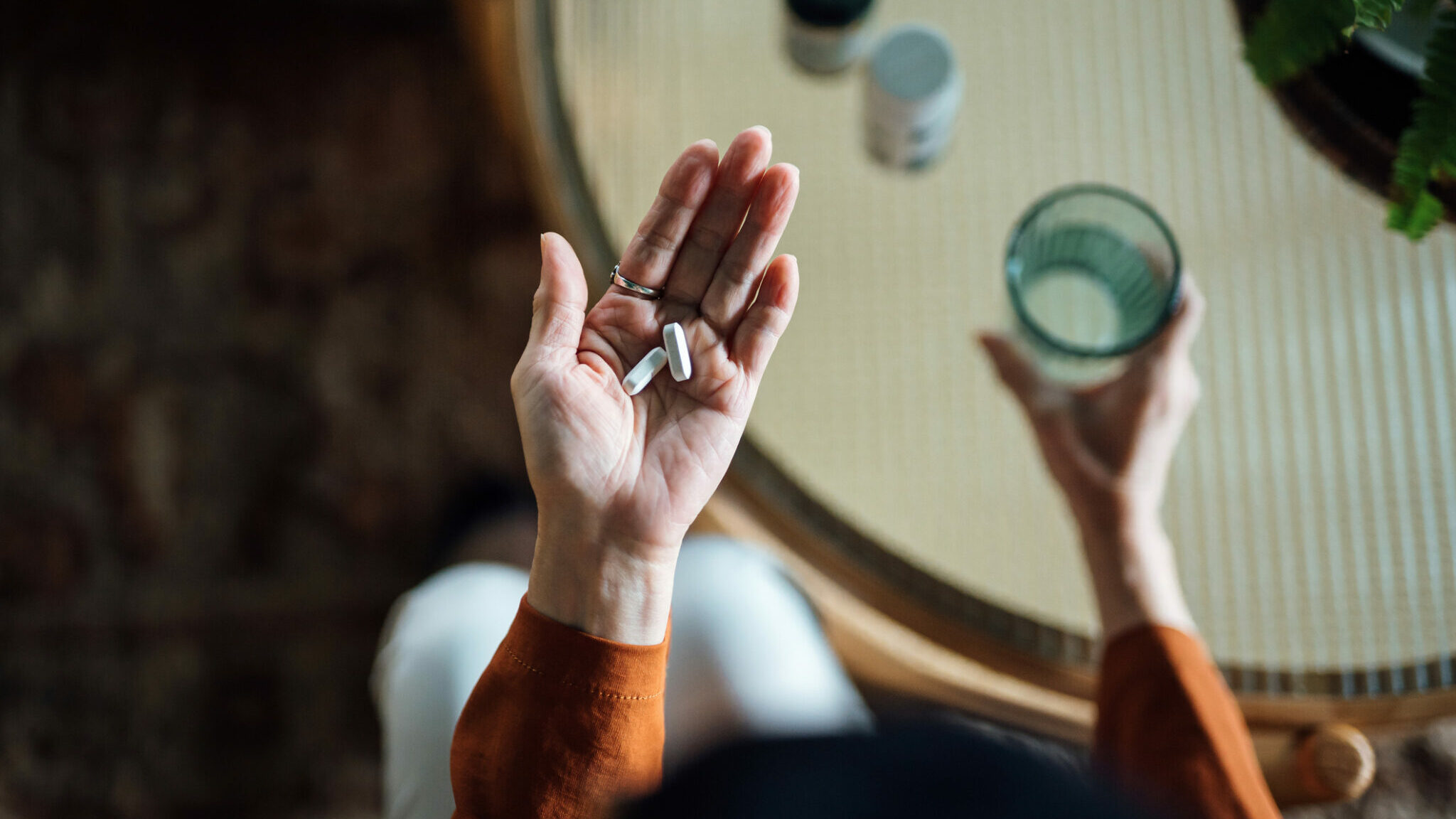 Overhead view of senior Asian woman feeling sick, taking medicines in hand with a glass of water at home. Elderly and healthcare concept alternate text for this image
