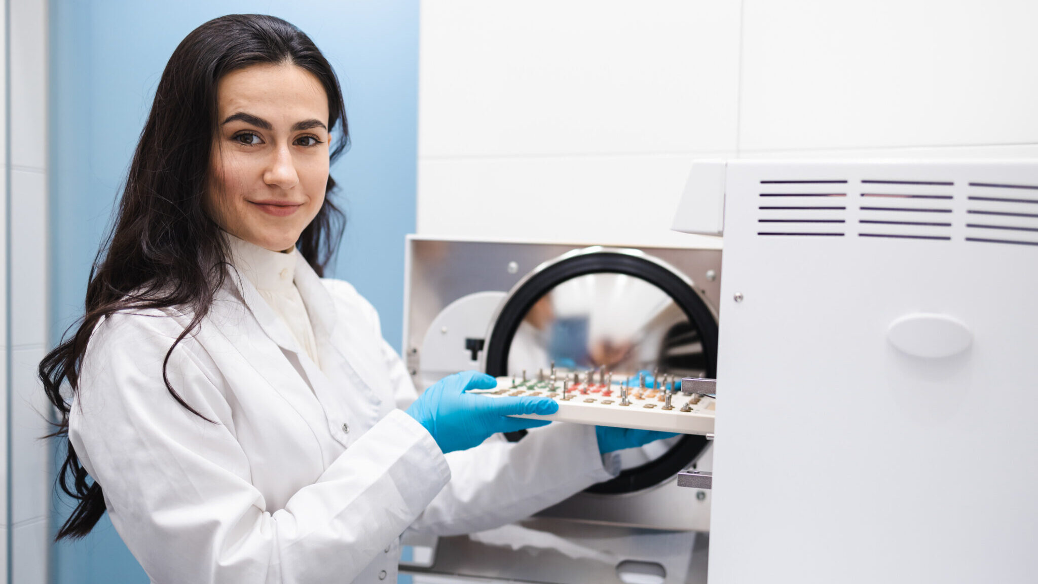 Young female assistant putting dental implant surgery set into autoclave. Sterilization of stomatology instruments alternate text for this image