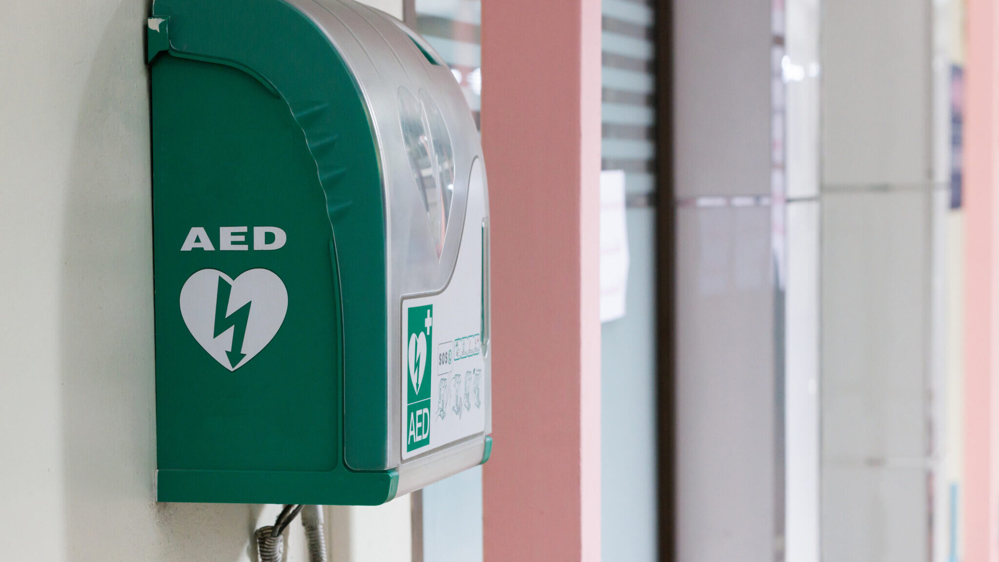 Automated external defibrillator in green box hang on wall in hospital. AED medical first aid device. alternate text for this image