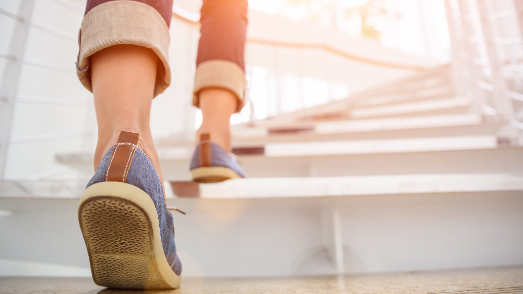 Young adult woman walking up the stairs with sun sport background. alternate text for this image