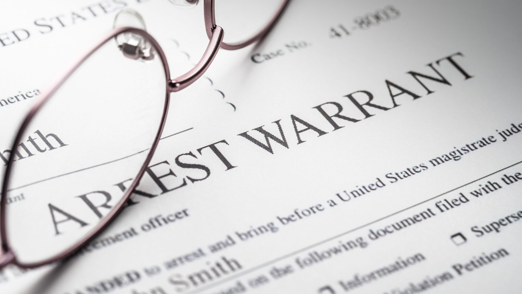 Arrest Warrant document with reading glasses alternate text for this image