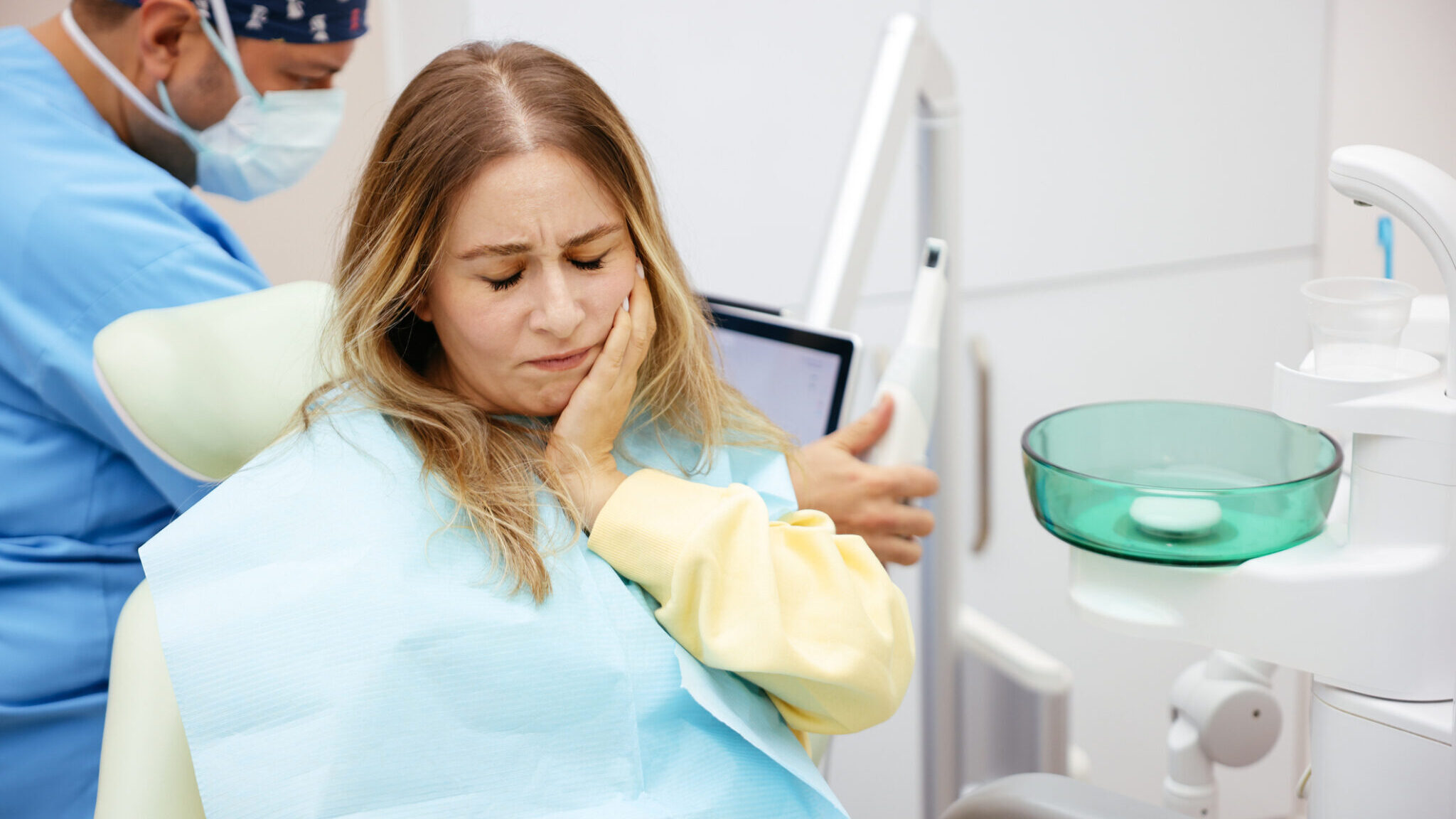 Young woman feeling pain, holding her cheek with hand at dentist’s office.Toothache concept. alternate text for this image