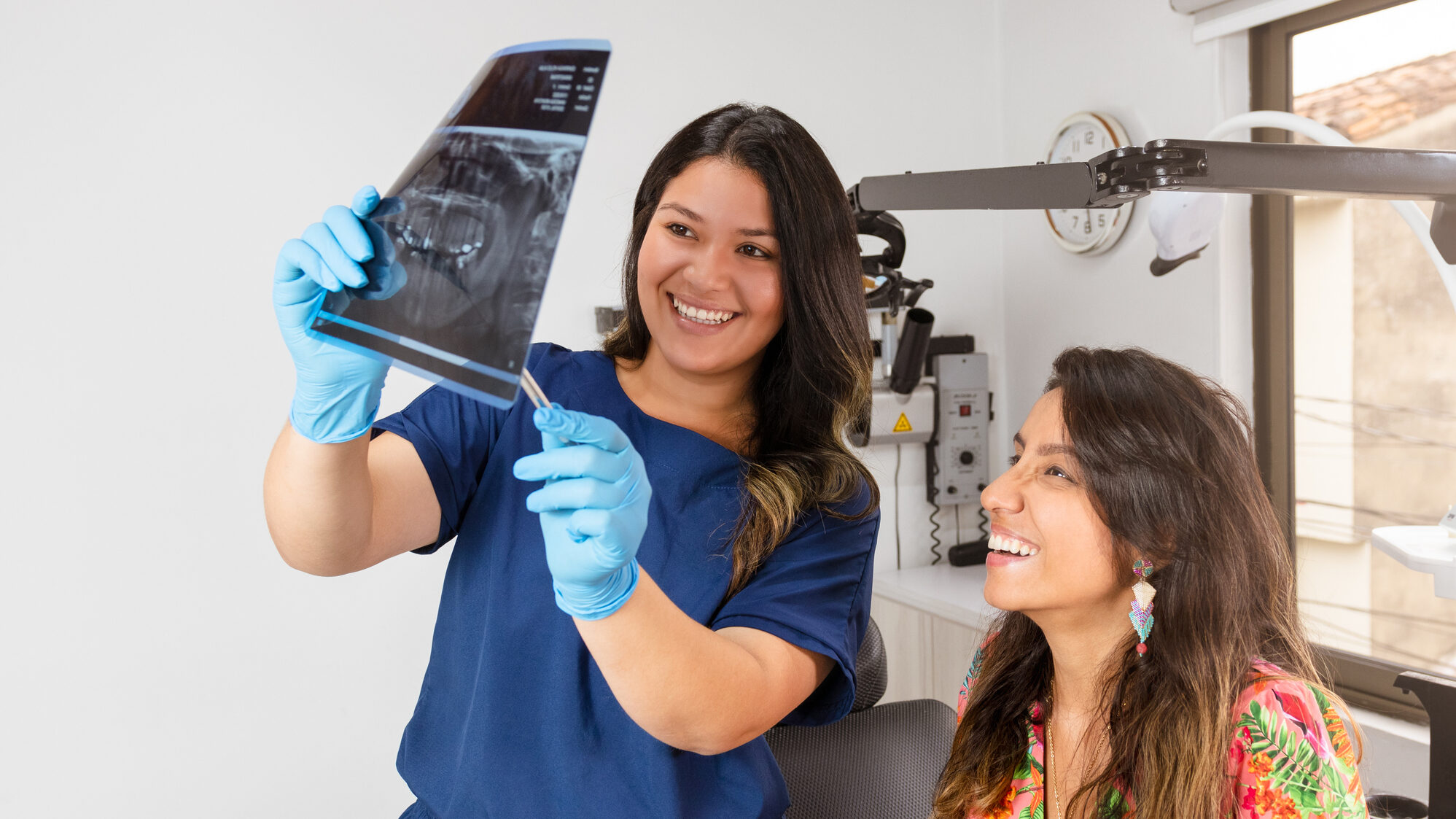 An experienced dentist smiles at her patient in the office while showing a panoramic X-ray for examination alternate text for this image