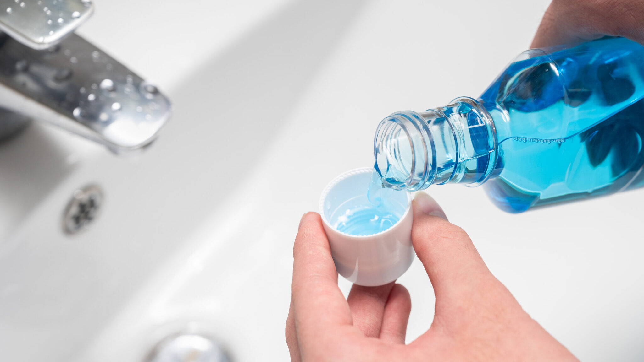 Hand of man Pouring Bottle Of Mouthwash Into Cap. alternate text for this image