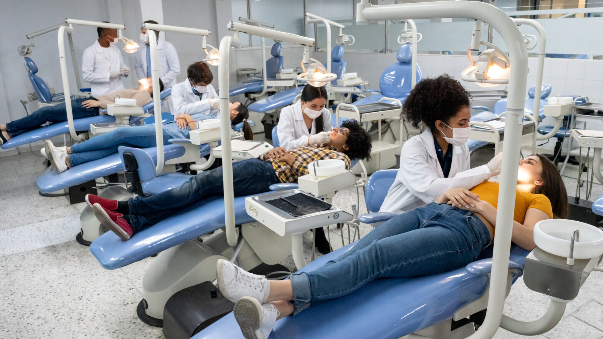 Students at dental school examining the teeth of some patients alternate text for this image
