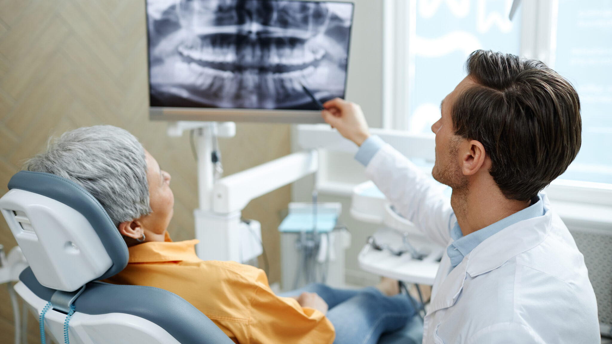 Back view of male dentist pointing at tooth X-ray image on screen alternate text for this image