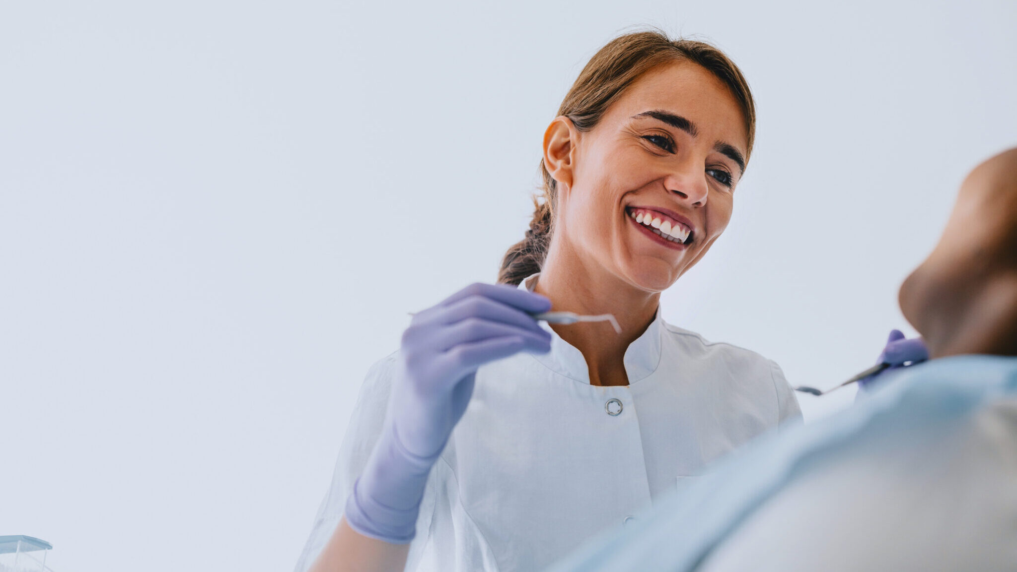 Female Dentist Smiling While Treating a Patient in Clinic alternate text for this image
