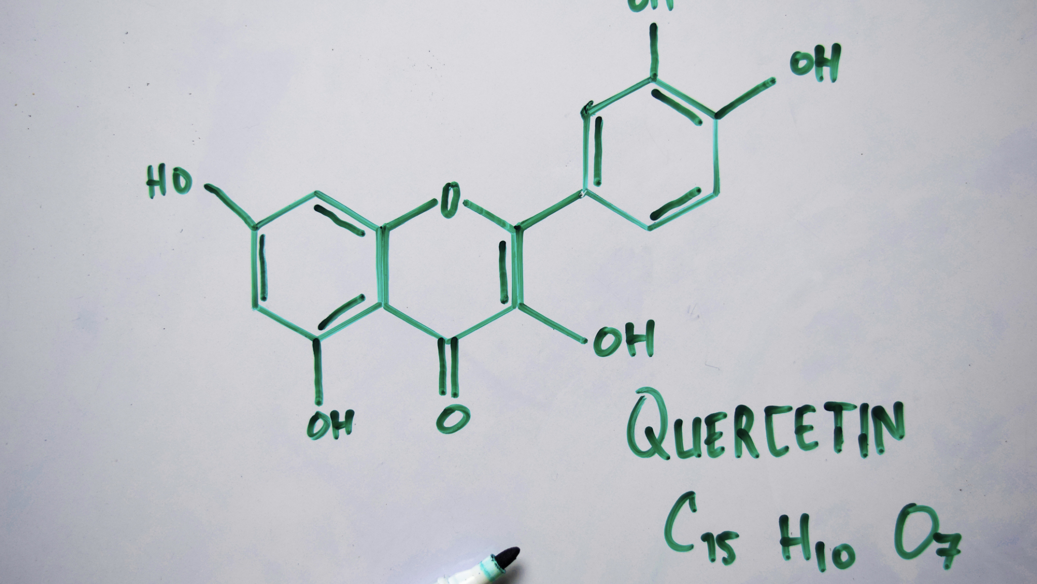 Structural formula of quercetin (C15H10O7) written on a whiteboard. The plant compound is being studied for its potential role in treating periodontal disease.