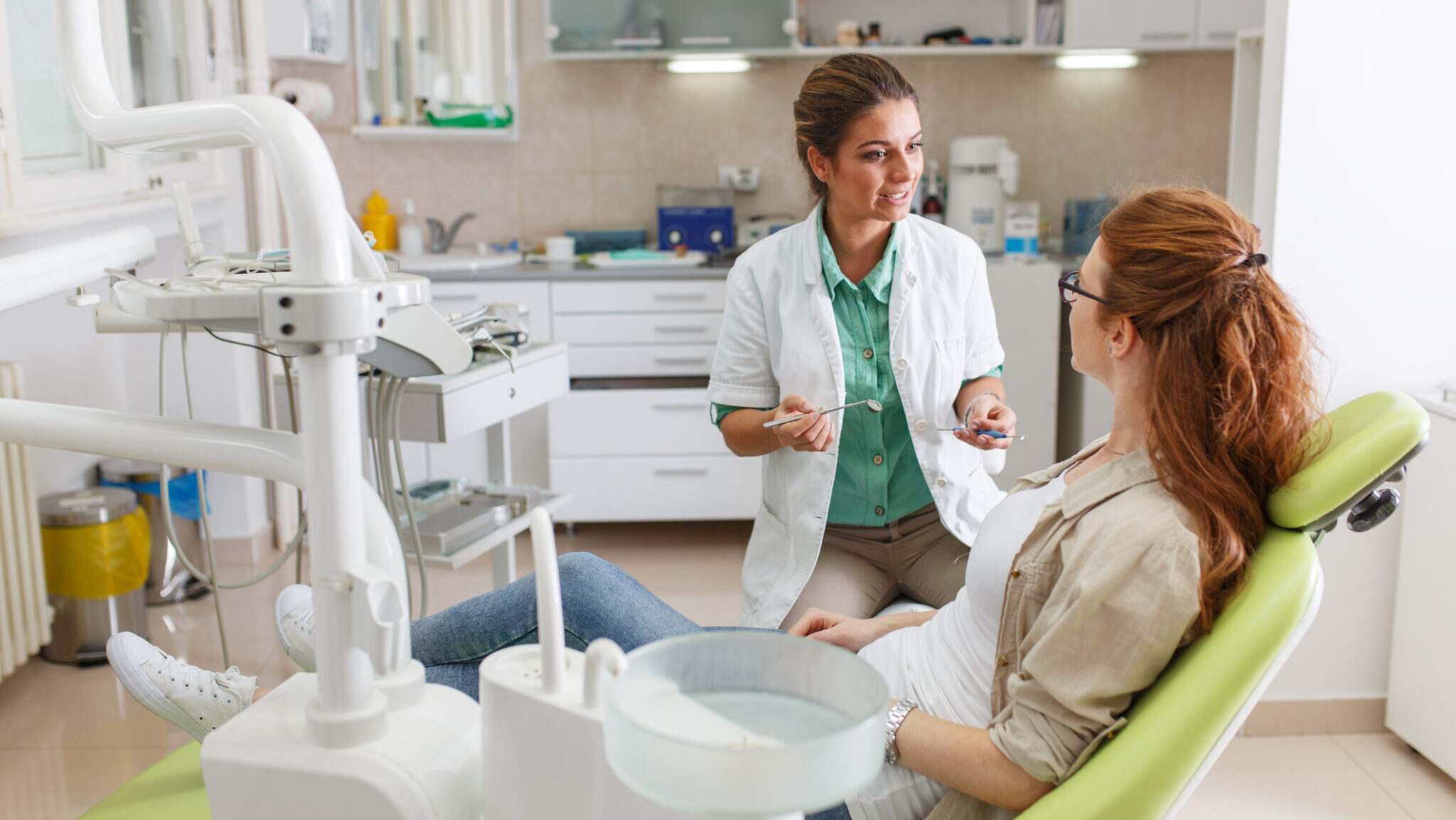 Female dentist in dental office talking with female patient and preparing for treatment.