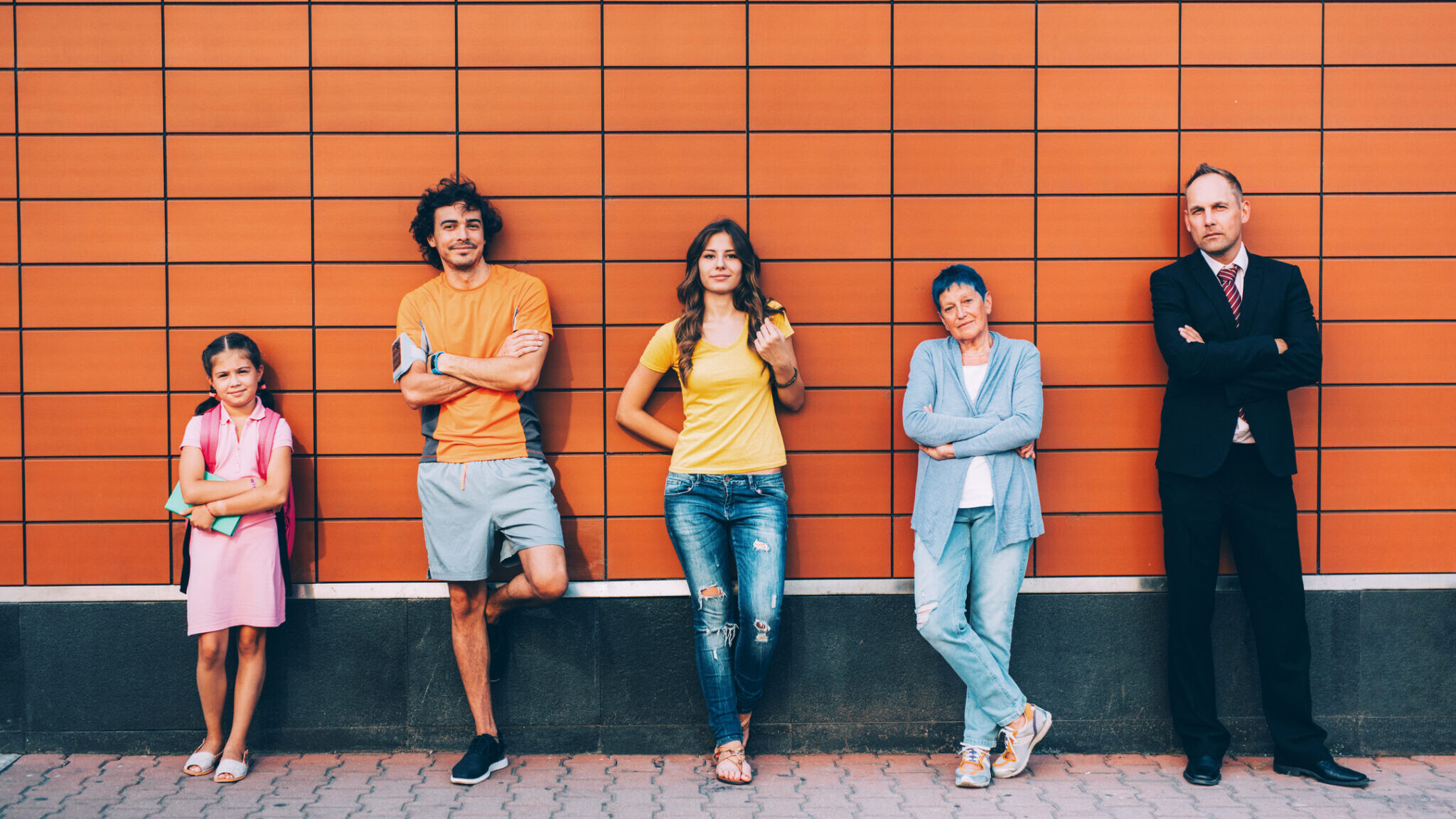 Five people at different ages standing against a wall separately.