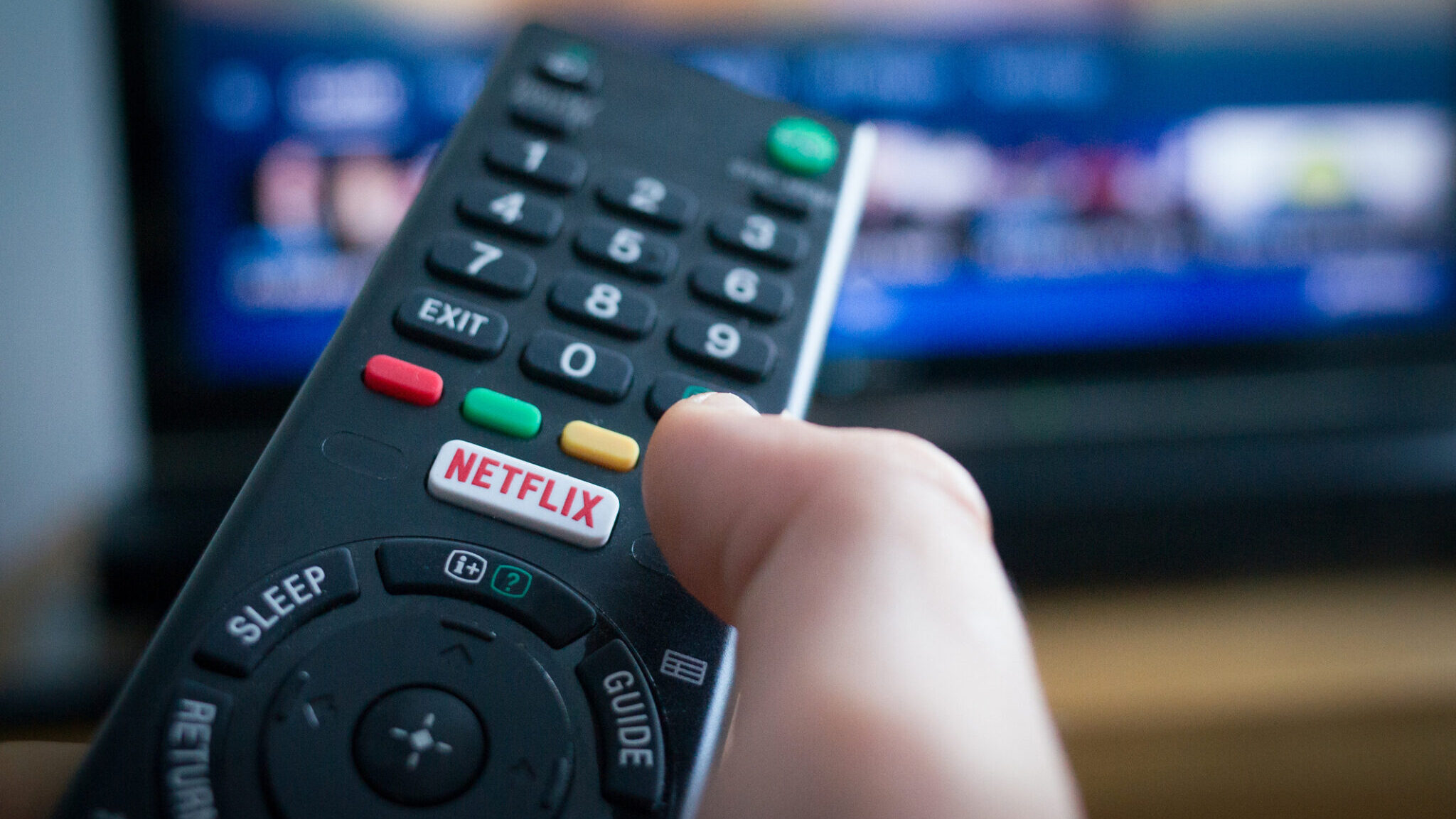 Using a television remote control with dedicated Netflix button, TV in the background.