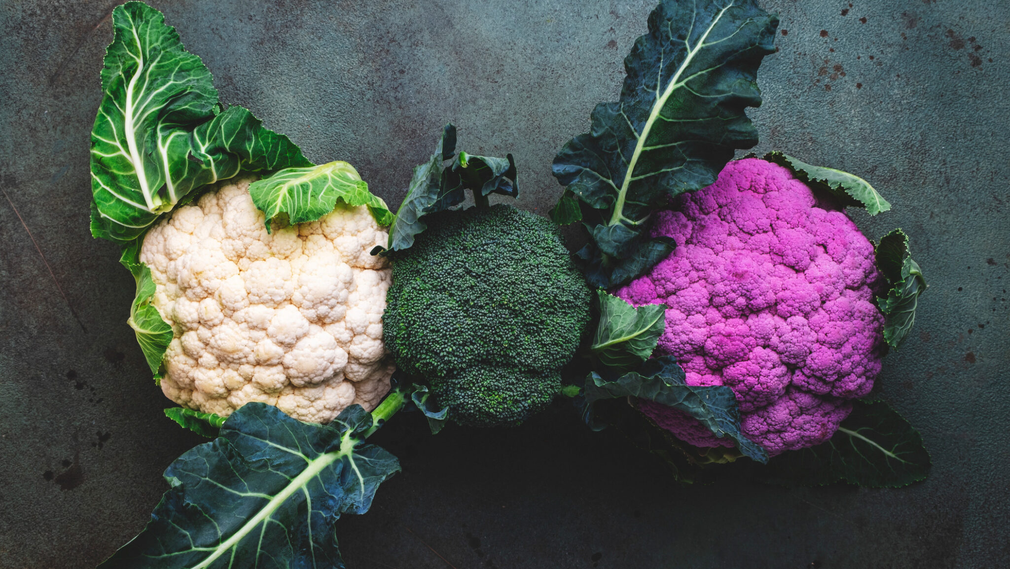 White and lilac cauliflower, broccoli cabbage from farm market on old rustic green table alternate text for this image