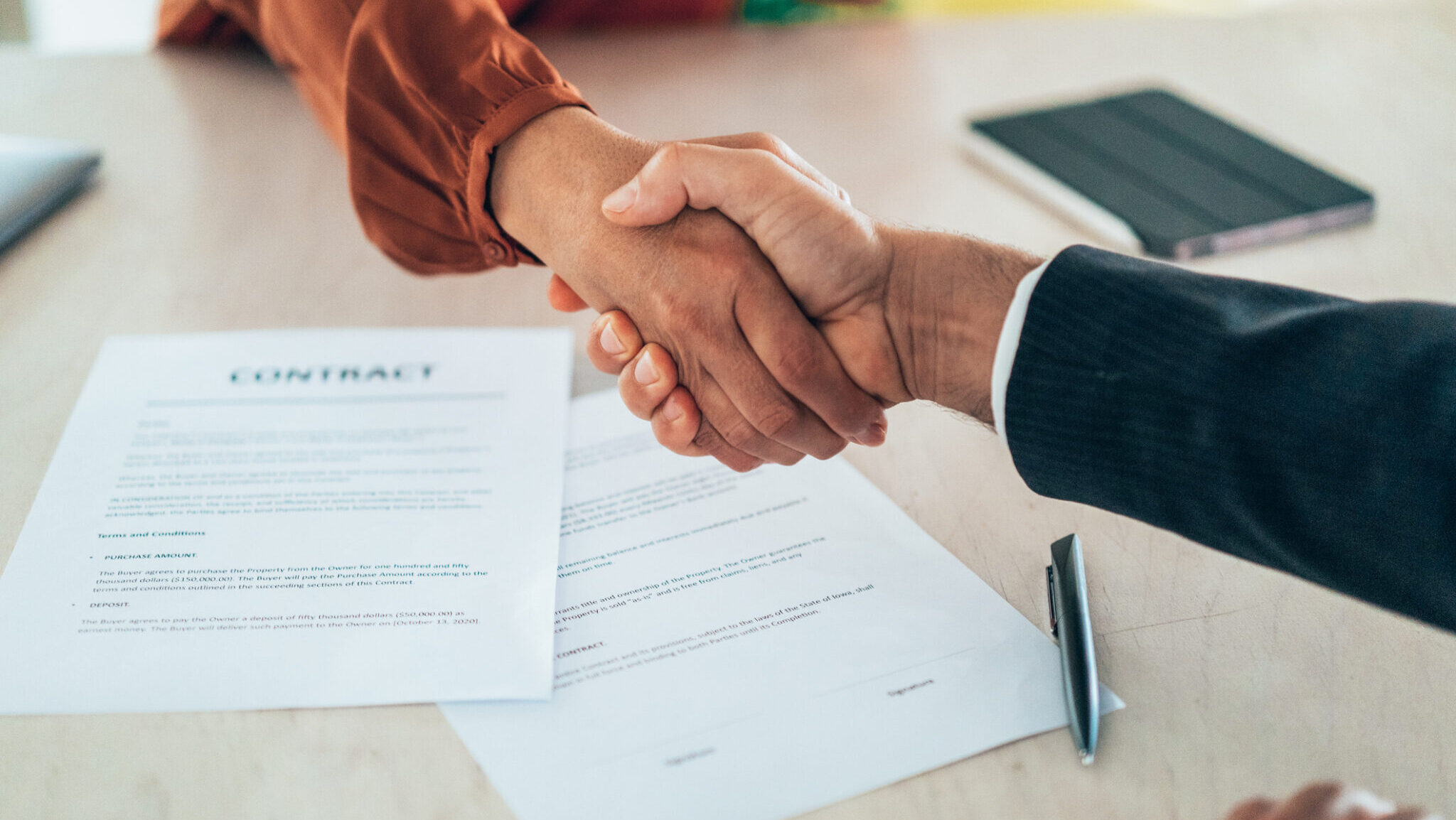Two professionals shake hands over a signed contract, representing the successful conclusion of a business deal. This image embodies the spirit of collaboration and trust in a corporate environment.
