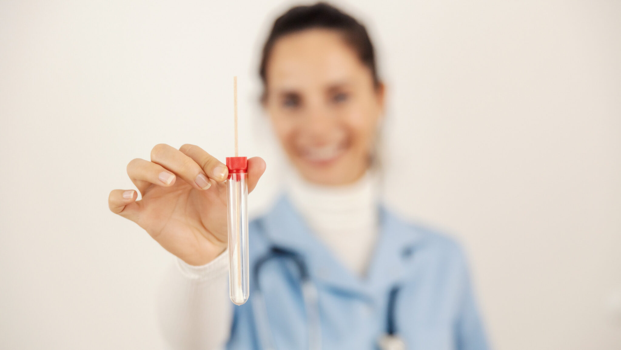 Selective focus on doctor’s hand holding cotton swab and showing it at camera. alternate text for this image