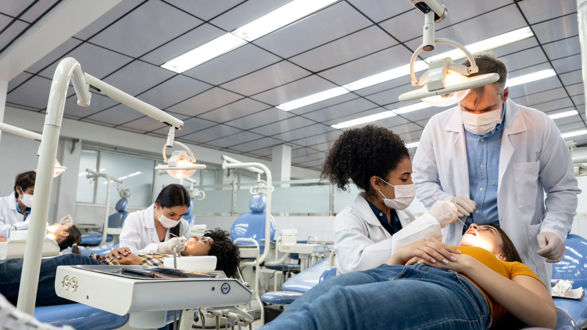 Student examining a patient at dental school under the supervision of a teacher. (iStock)