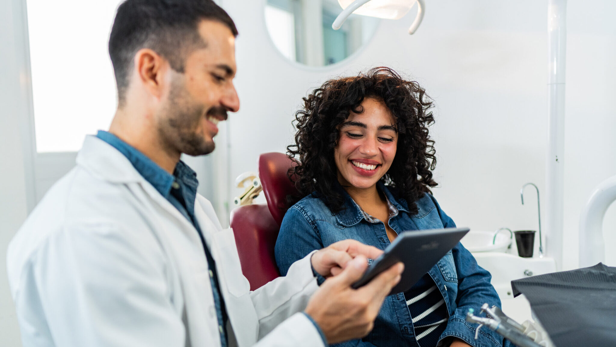 Mid adult dentist man using digital tablet and talking to young patient woman at dentist's office