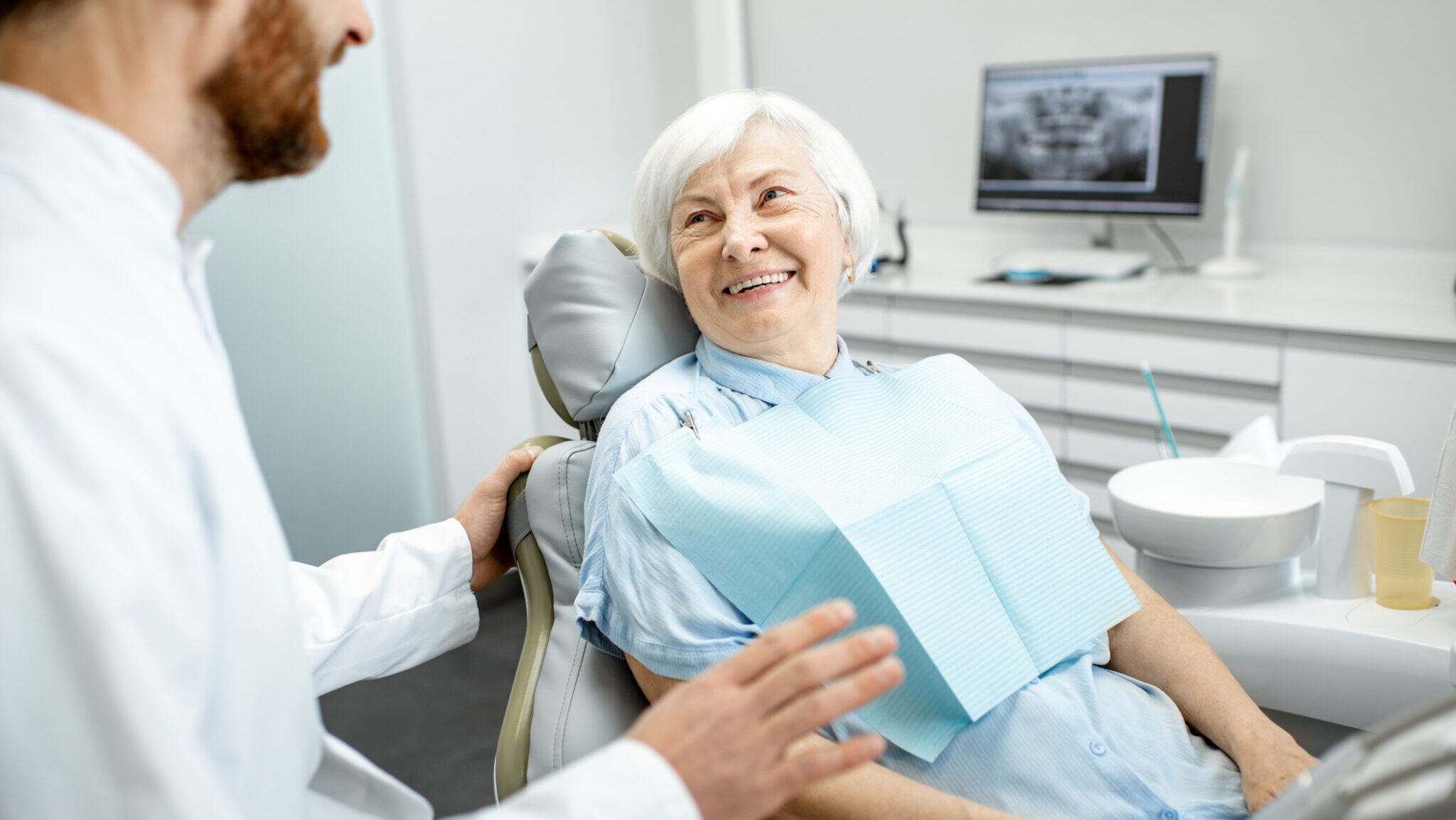 Beautiful elder woman with healthy smile sitting during the consultation with dentist at the dental office