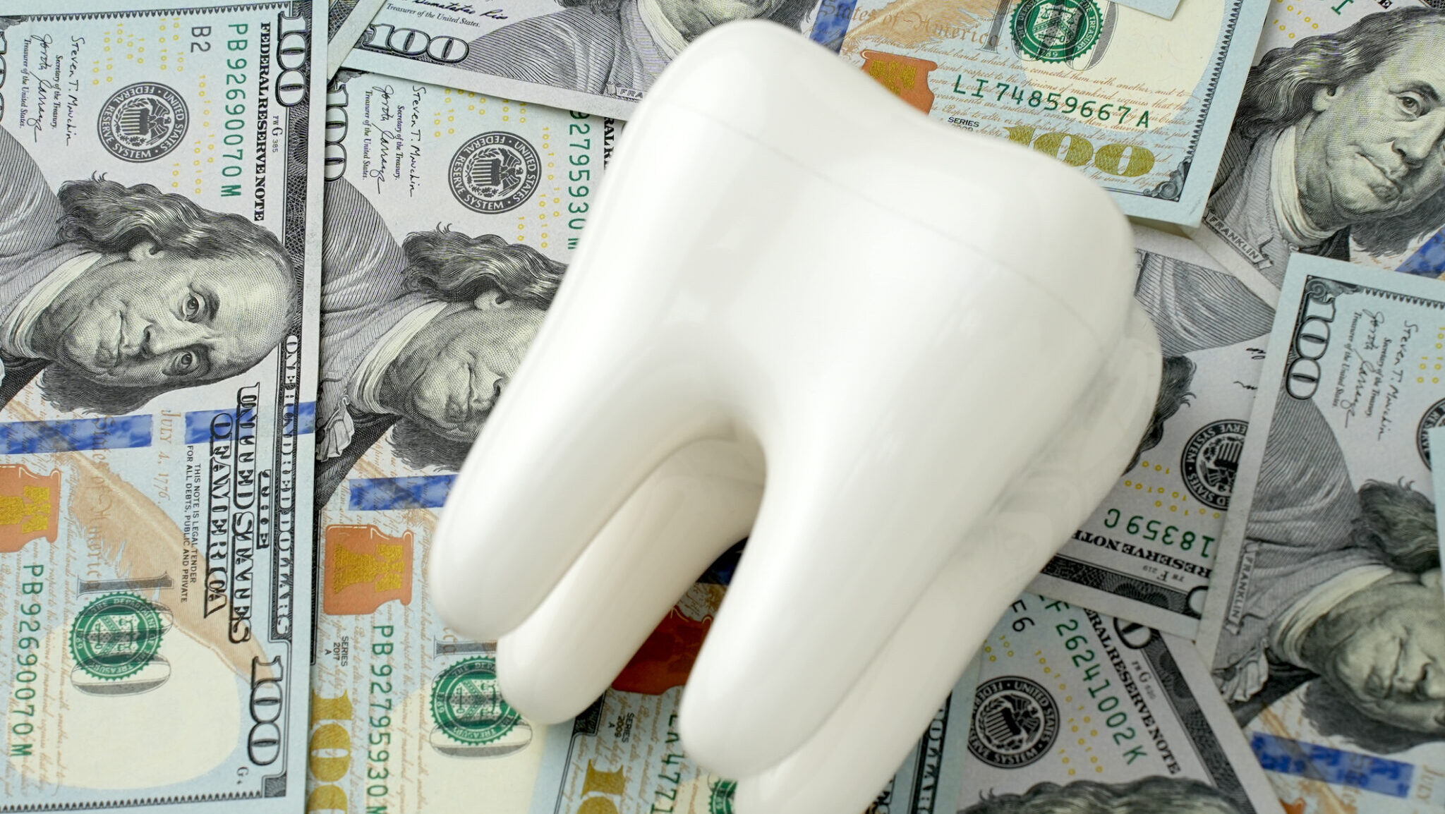 Concept expensive dentistry or dental insurance. Tooth model and money bills background, close-up